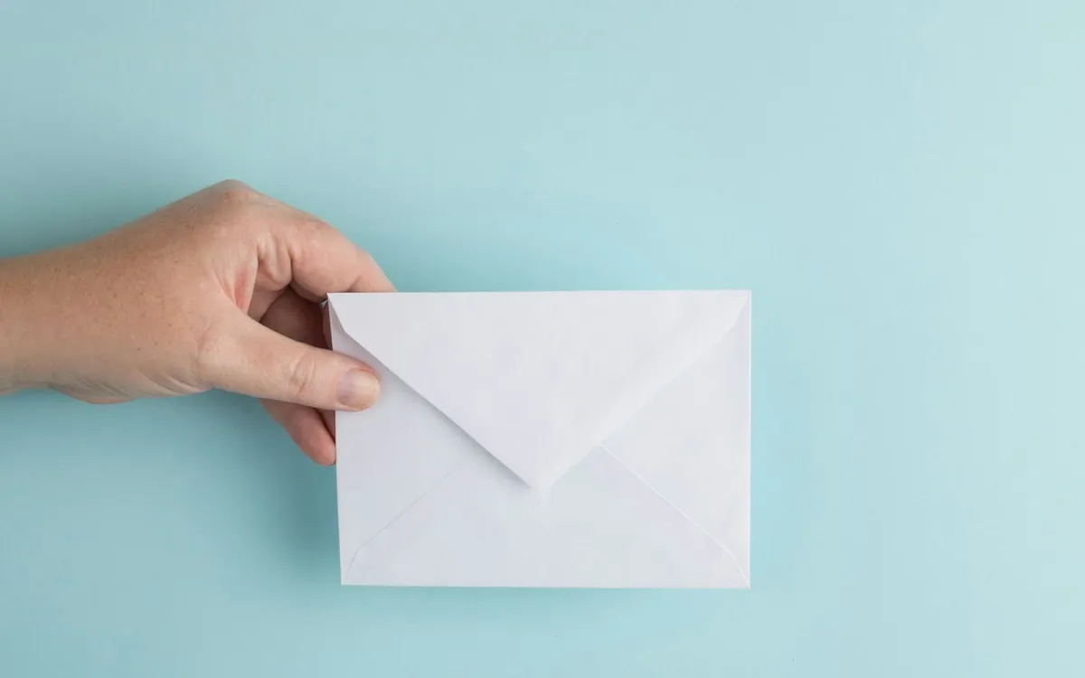 Mão segurando um envelope branco.